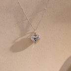 The white gold version of the Puff Heart Pendant Necklace displayed against a sand-colored background.