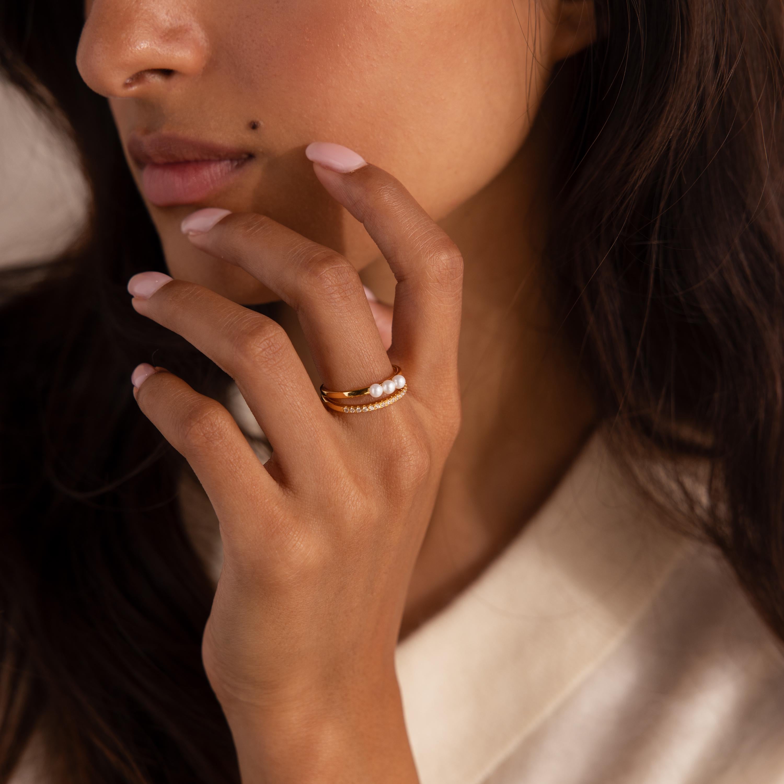 Woman wearing a duo band ring featuring a gold band with three small pearls and a pavé crystal band, styled with a soft cream top.