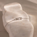 Delicate silver chain bracelet displayed on a textured stone surface, featuring an interlocking oval link design with one link encrusted in small clear stones.