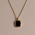 Gold chain necklace featuring a square black onyx pendant in a textured gold bezel, displayed against a neutral background with soft lighting.