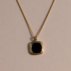 Gold chain necklace featuring a square black onyx pendant in a textured gold bezel, displayed against a neutral background with soft lighting.