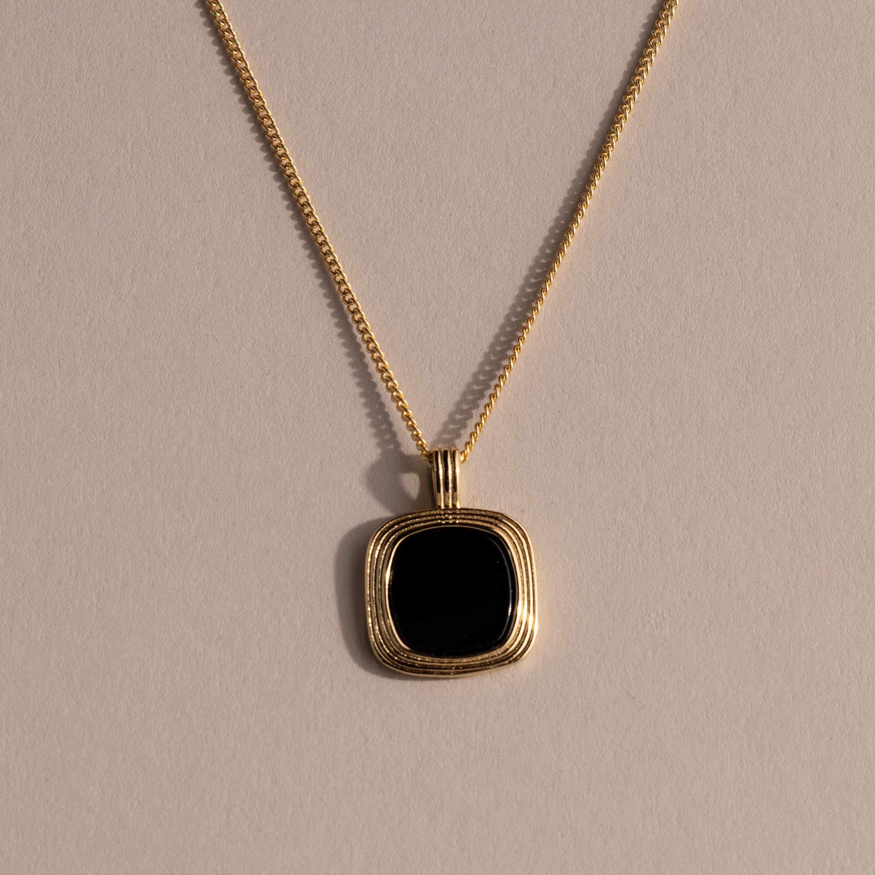 Gold chain necklace featuring a square black onyx pendant in a textured gold bezel, displayed against a neutral background with soft lighting.