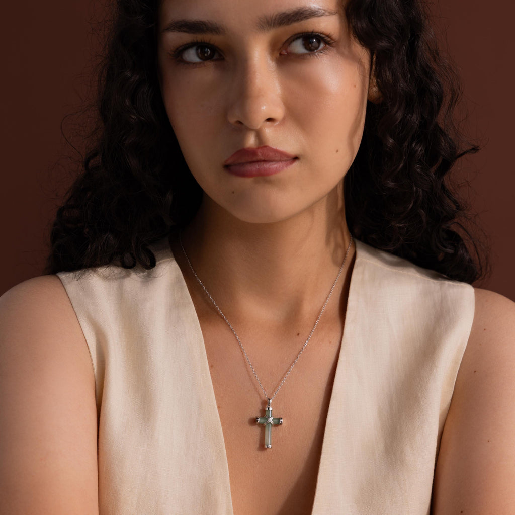 Woman wearing a silver chain necklace with a jade cross pendant, featuring polished silver end caps and an X-shaped detail at the center.