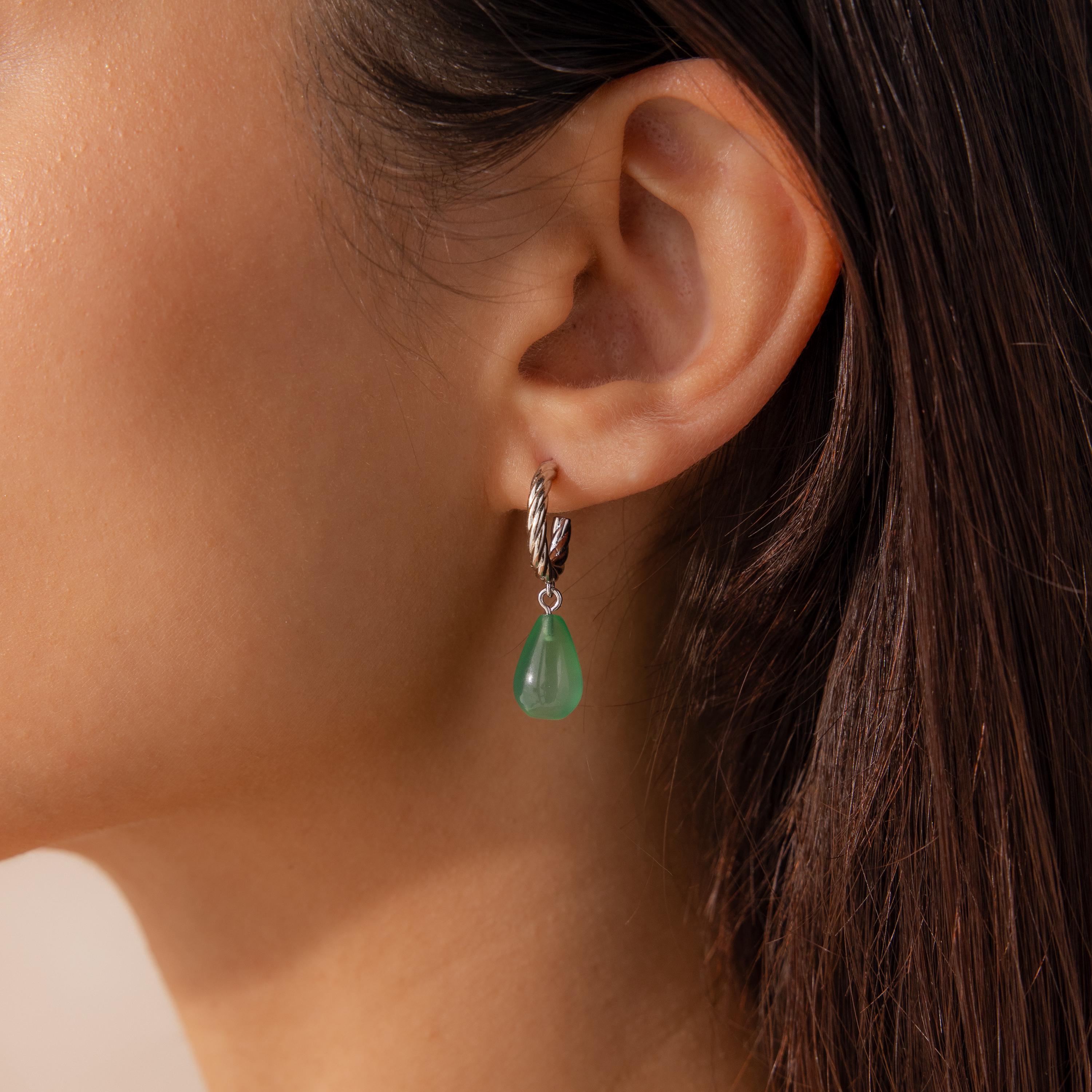 Green jade teardrop earring hanging from a twisted silver hoop worn on a model’s ear.