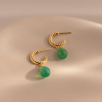 Twisted gold hoops with green jade drops elegantly hanging from a white ceramic vase.