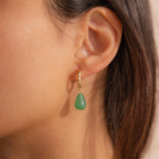 Green jade teardrop earring hanging from a twisted gold hoop worn on a model’s ear.