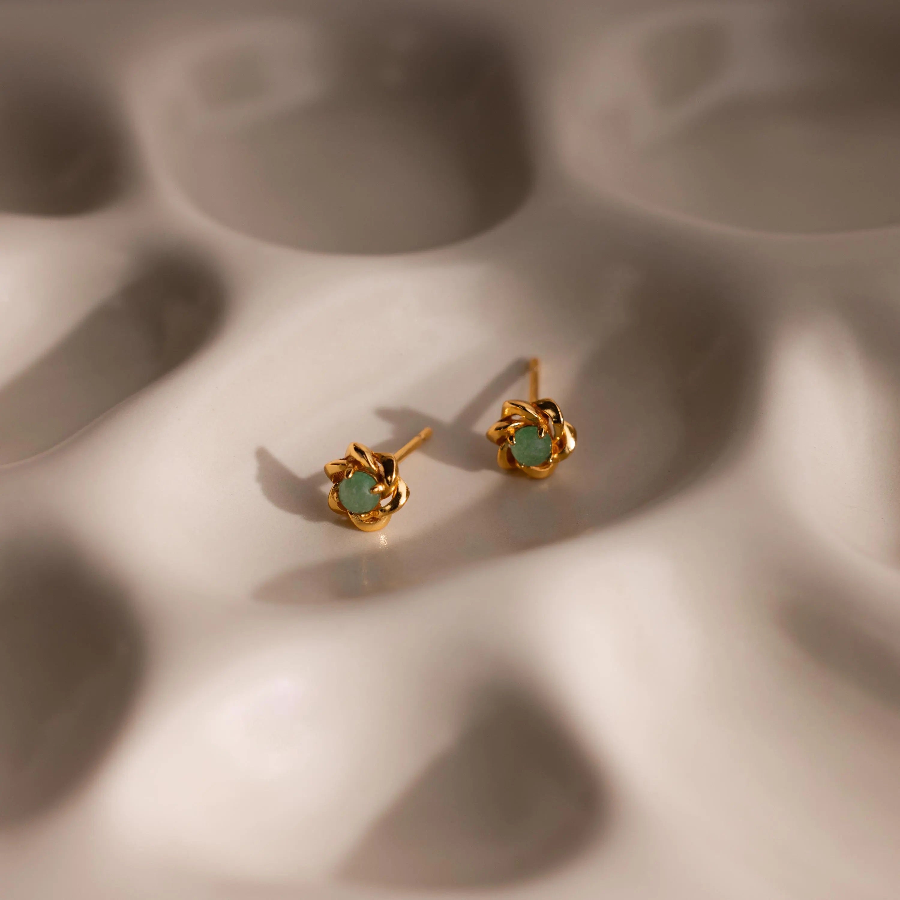 Close-up of gold flower-shaped jade stud earrings with a round jade gemstone center.
