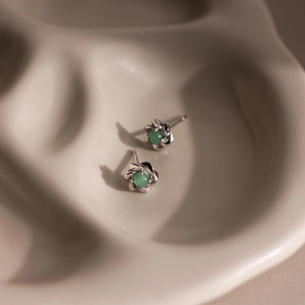 Flay-lay of silver flower-shaped stud earrings with a round green jade gemstone center.