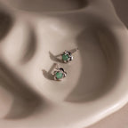 Flay-lay of silver flower-shaped stud earrings with a round green jade gemstone center.