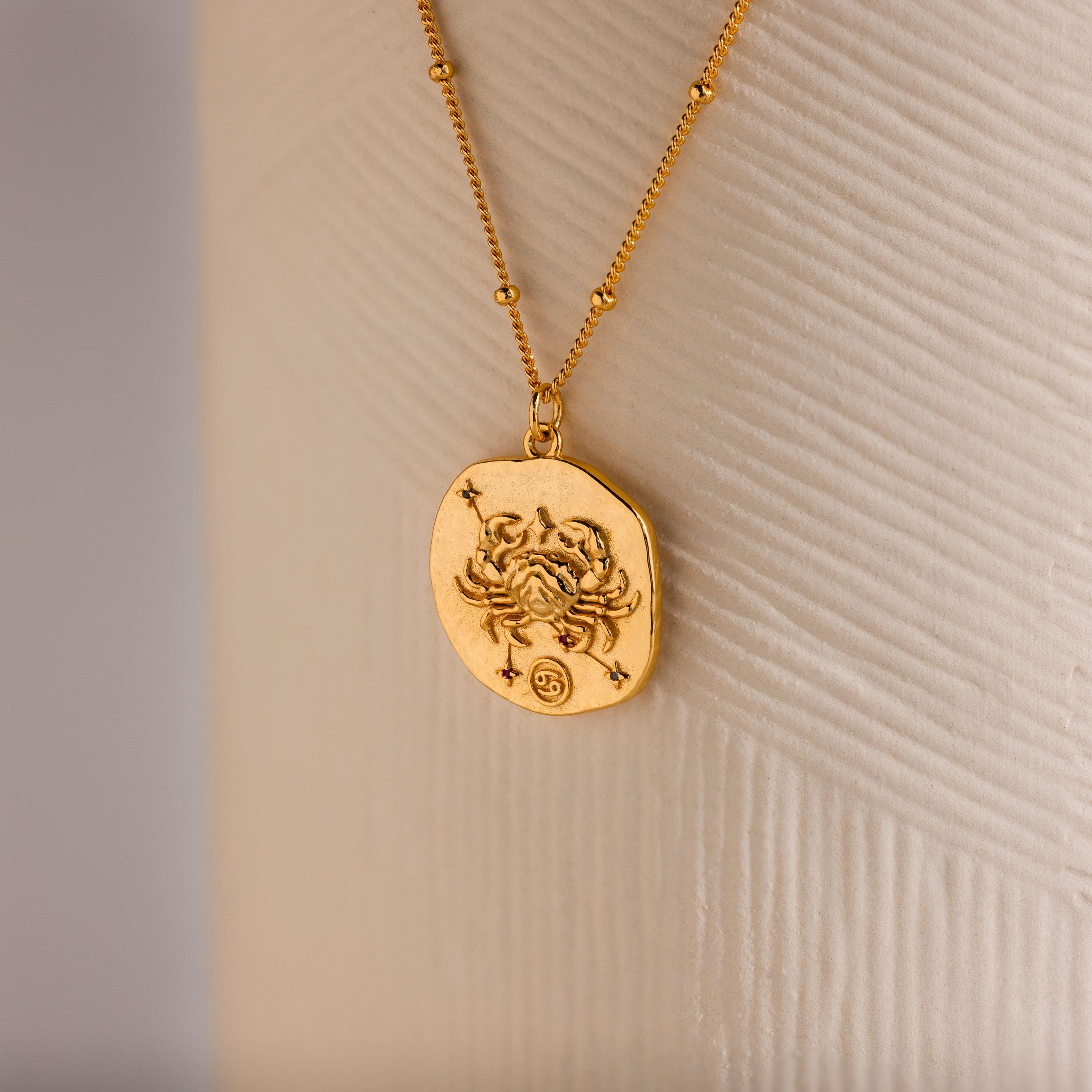 Close up of a Gold 3D Cancer Zodiac Coin Pendant Necklace with small CZ gemstones, attached to a dainty satellite chain.
