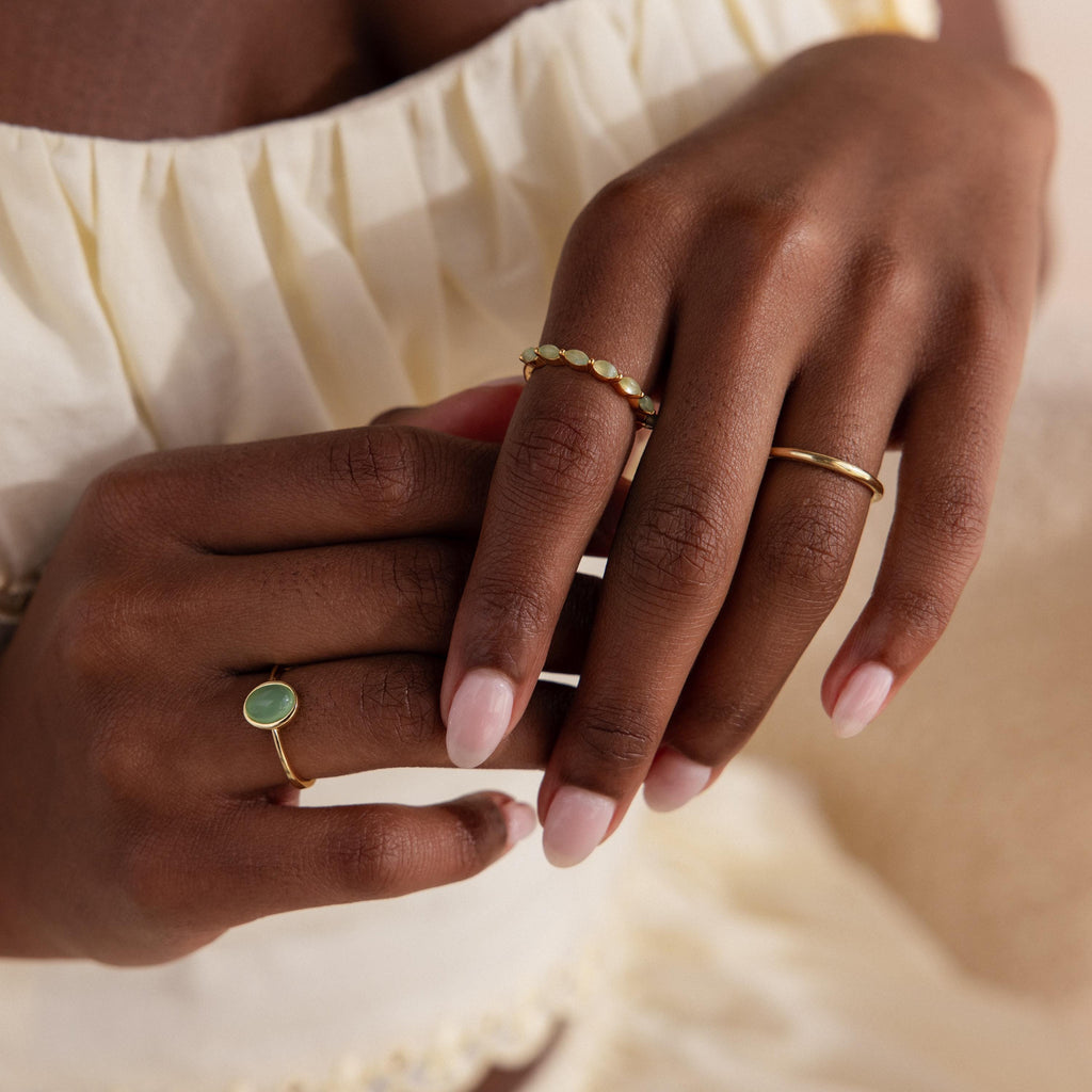 Two hands elegantly posed wearing a selection of gold rings, with the marquise jade ring featured prominently alongside other minimalist styles.