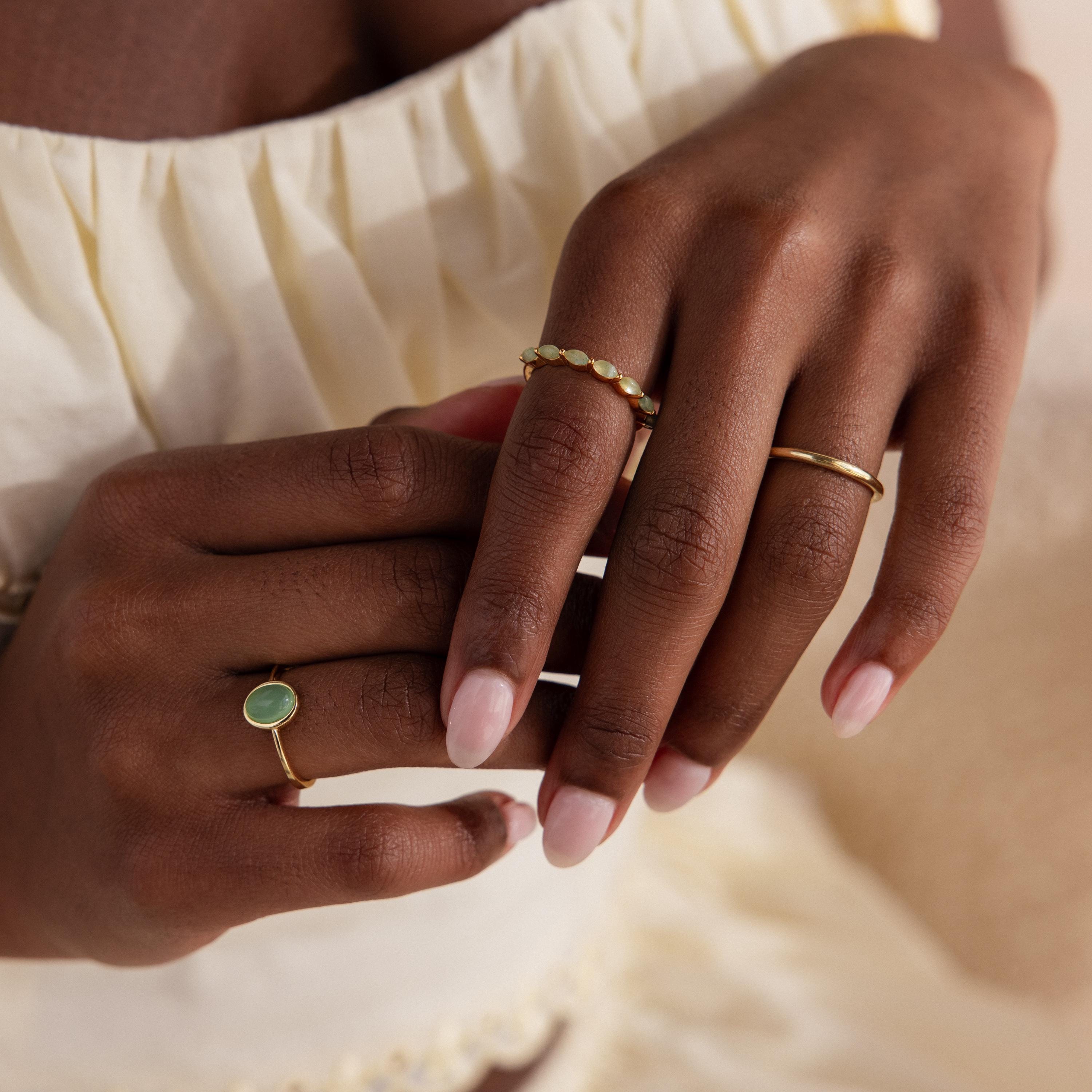 Two hands elegantly posed wearing a selection of gold rings, with the marquise jade ring featured prominently alongside other minimalist styles.