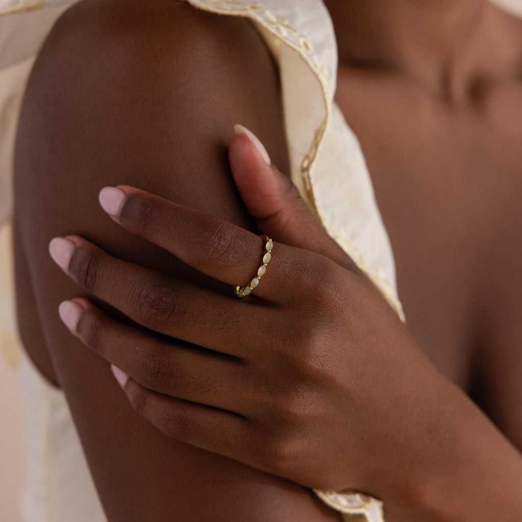 A model resting her hand on her shoulder, showcasing the marquise jade ring on her index finger, styled with a cream ruffled top.