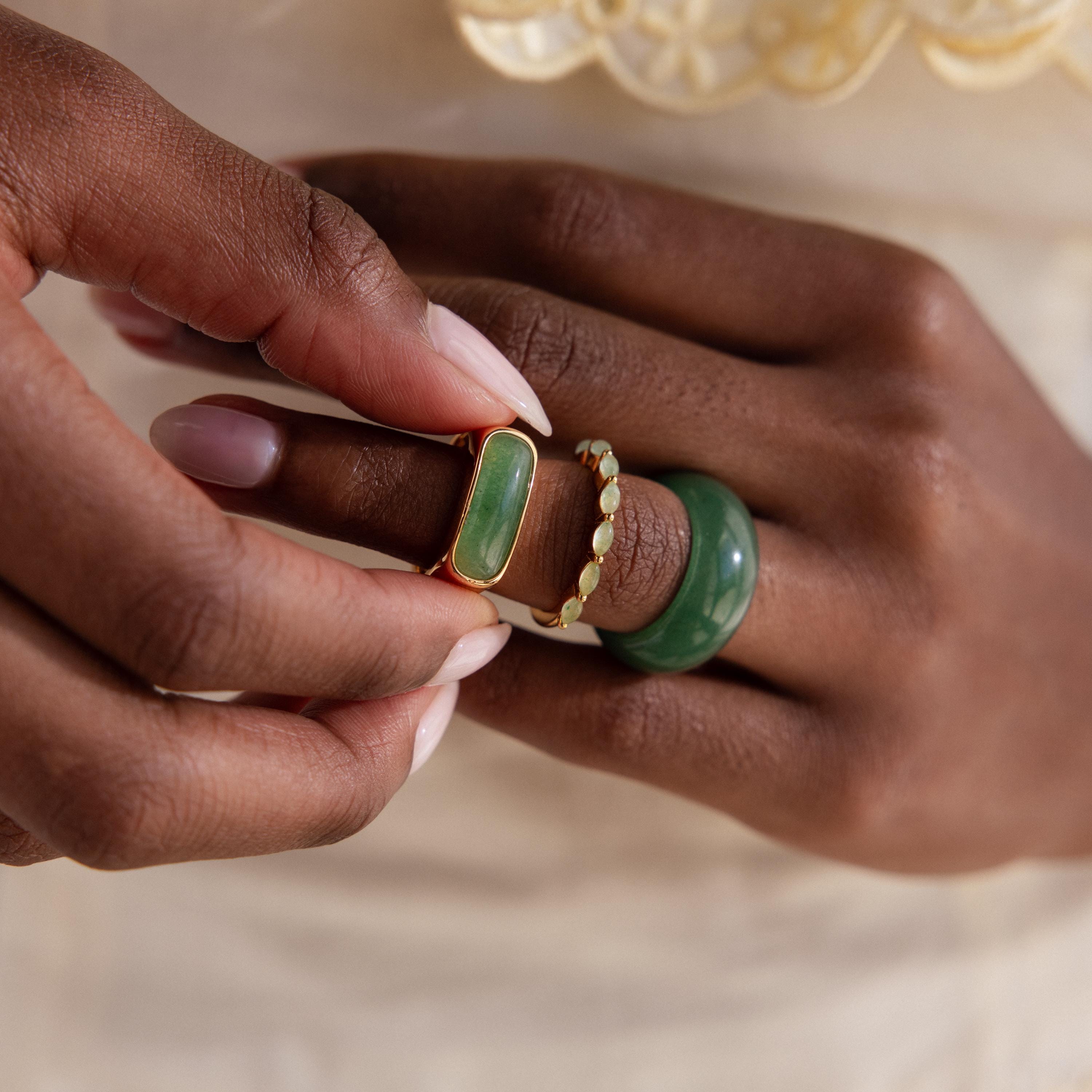 Close-up of a hand wearing a stack of jade rings, including a marquise jade ring set in gold, paired with two other green gemstone rings.