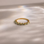 Golden marquise jade ring placed on a soft satin surface, surrounded by dreamy natural lighting and subtle rainbow reflections.