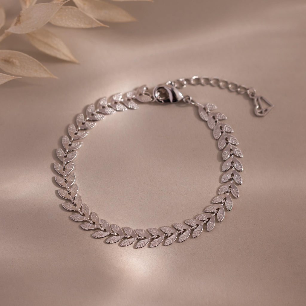 Flat-lay of a white gold leaf link chain bracelet with textured leaf-shaped links displayed on a neutral surface.