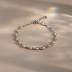 Silver chain bracelet with evenly spaced white pearls, featuring an adjustable clasp and heart-shaped detail, displayed on a neutral surface with soft light reflections.