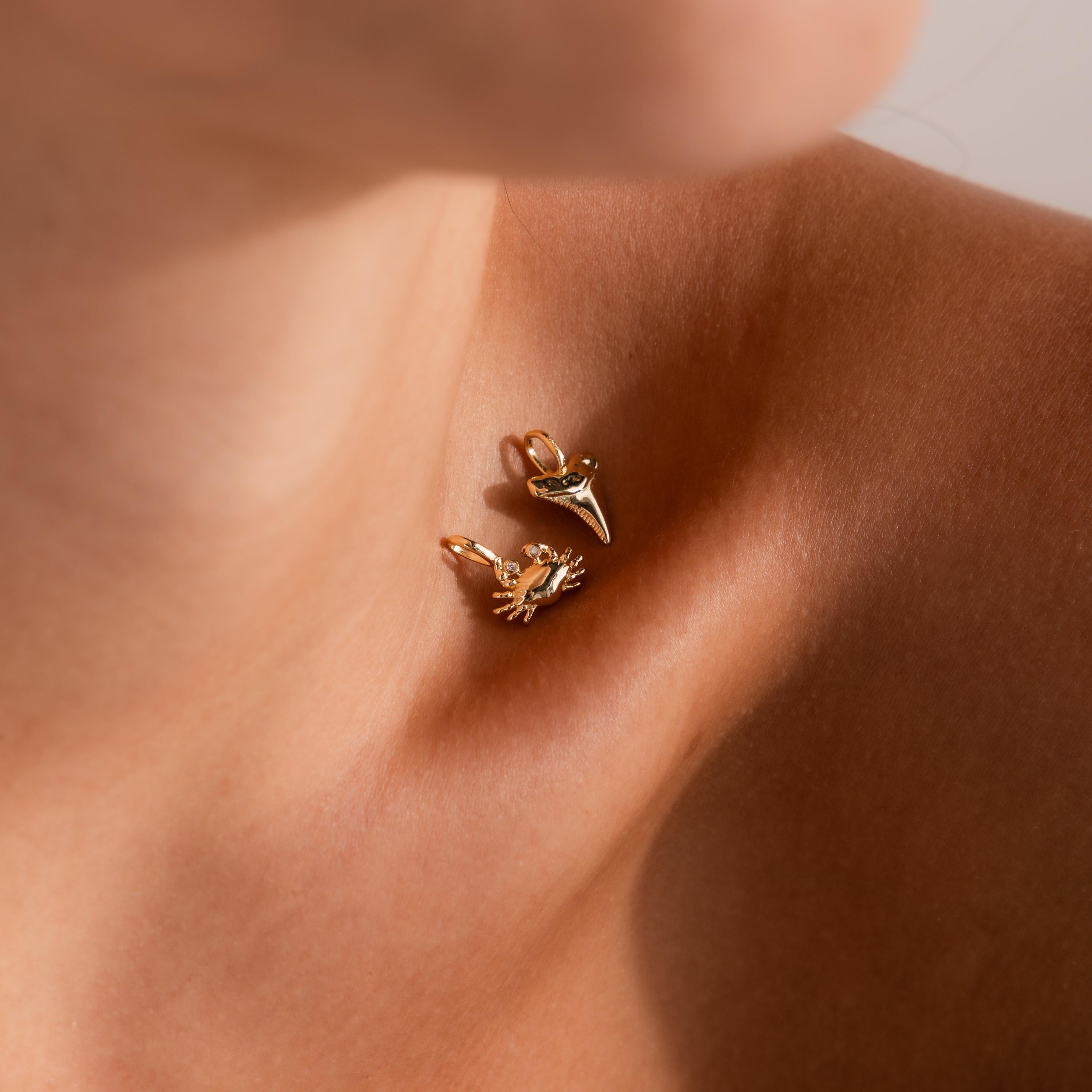 Gold crab charm with gemstone eyes and gold shark tooth charm styled on skin for a coastal-inspired jewelry look.
