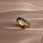Single gold eternity ring displayed upright on a neutral surface, featuring marquise cut stones in a blue ombre gradient from deep navy to pale sky blue.