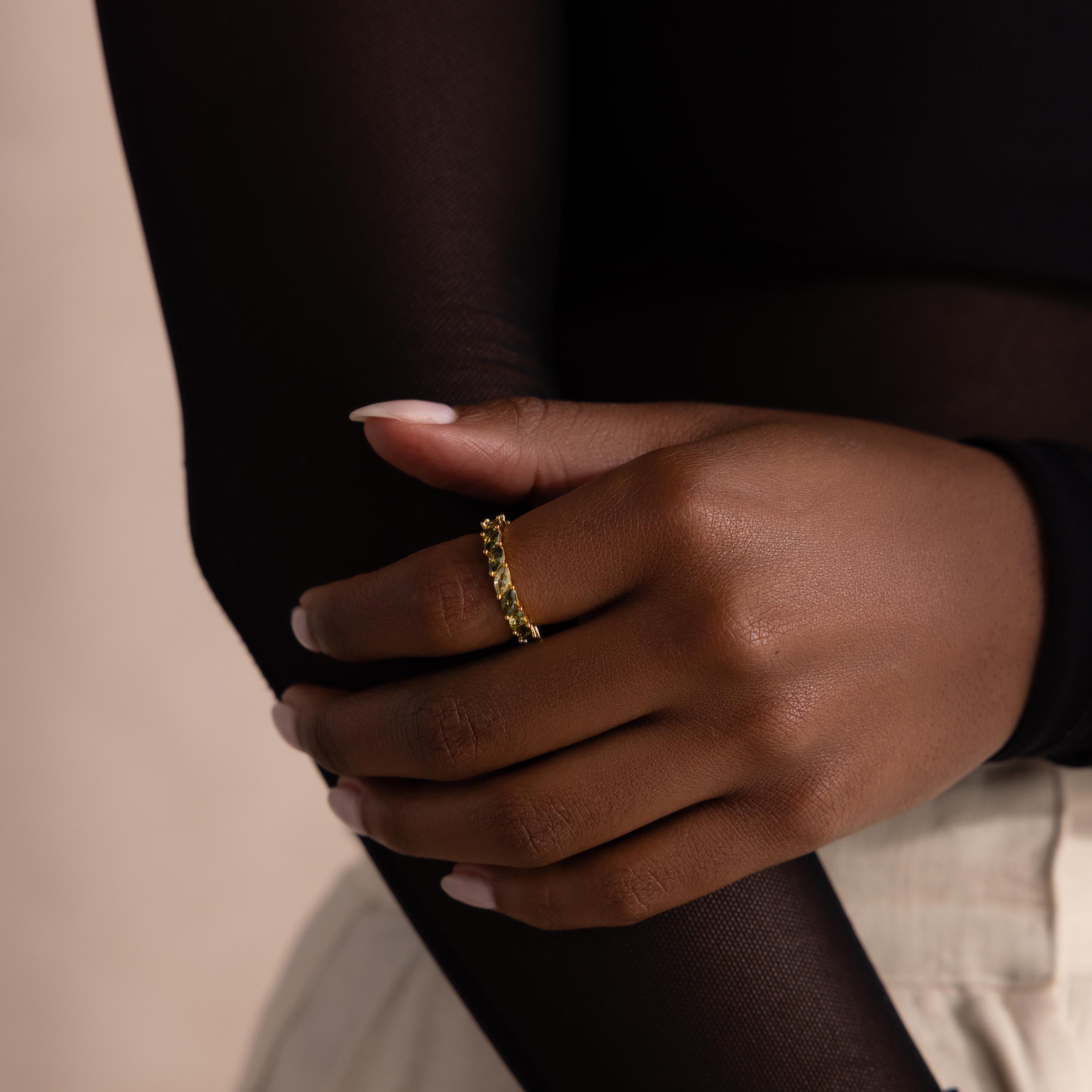 Model wears a gold eternity band on her finger, set with ombre green marquise cut stones that transition from pale mint to deep olive. Her hand rests gently on her opposite arm.