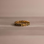 Marquise cut eternity ring with ombre green gemstones fading from deep olive to pale mint, set in a continuous gold band and displayed on a soft neutral surface.