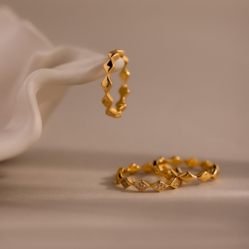 Set of 3 eternity curve rings in gold, featuring quilted design with one diamond-accented band, elegantly displayed on soft neutral fabric.