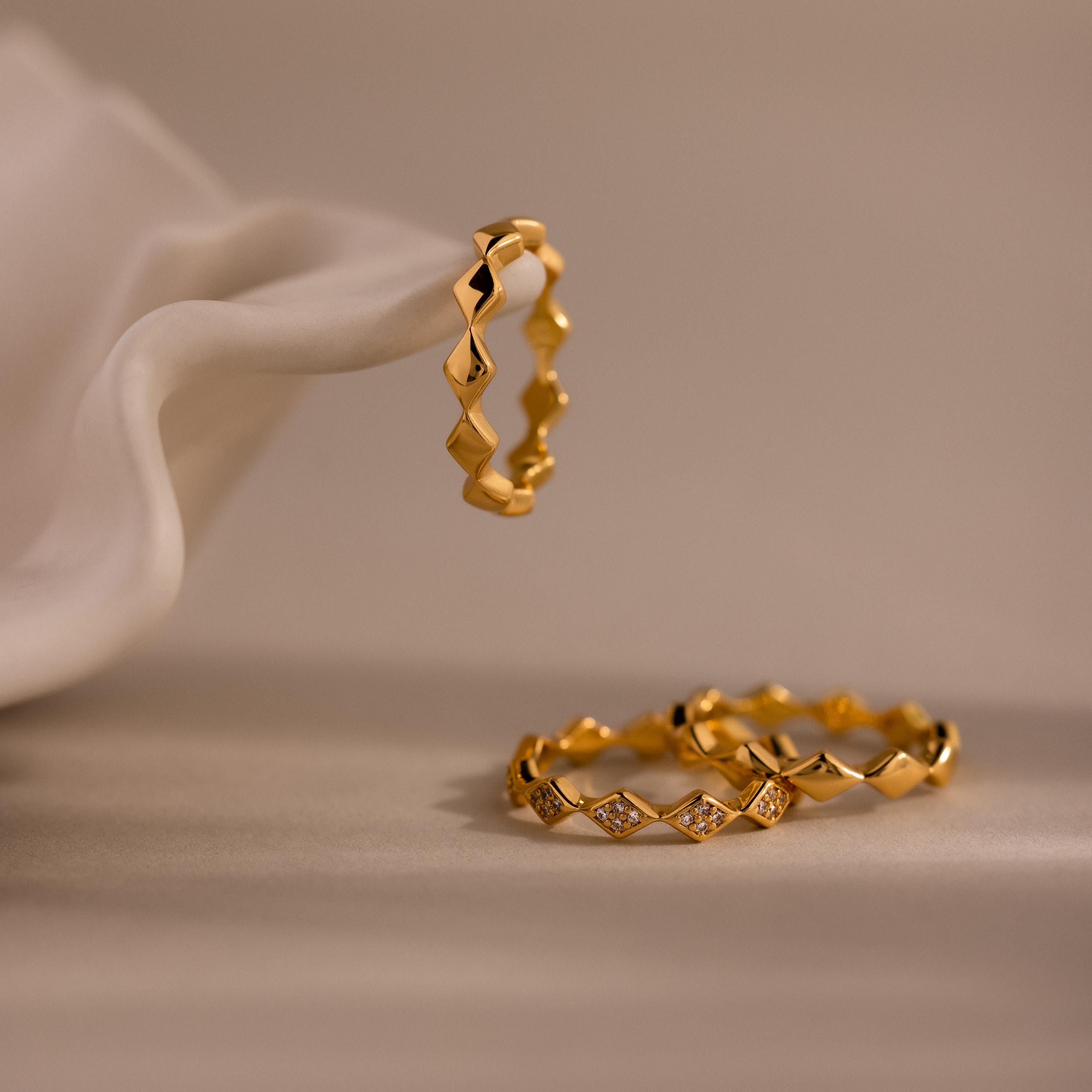 Set of 3 eternity curve rings in gold, featuring quilted design with one diamond-accented band, elegantly displayed on soft neutral fabric.