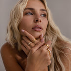 Woman wearing multiple statement rings, including a stacked set of gold eternity curve rings with quilted design and diamond accents, styled with other gold and crystal rings.