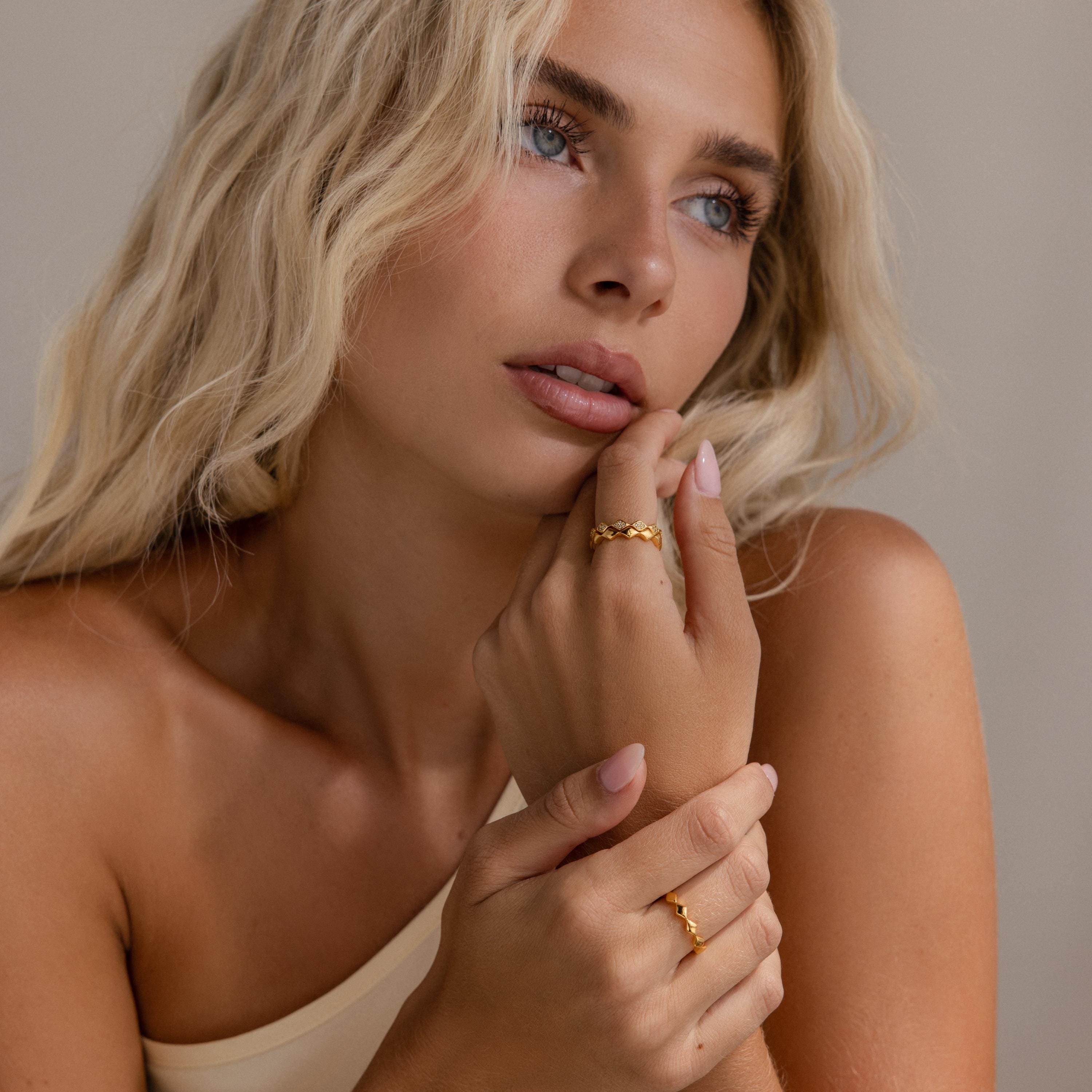 Woman wearing a set of 3 eternity curve rings in gold, including quilted bands with diamond accents, styled with soft waves and neutral attire.
