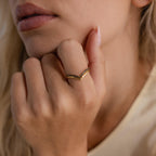 Close-up of a woman wearing a gold curve ring set, featuring one smooth band and one pavé band with black stones, styled together on her finger.