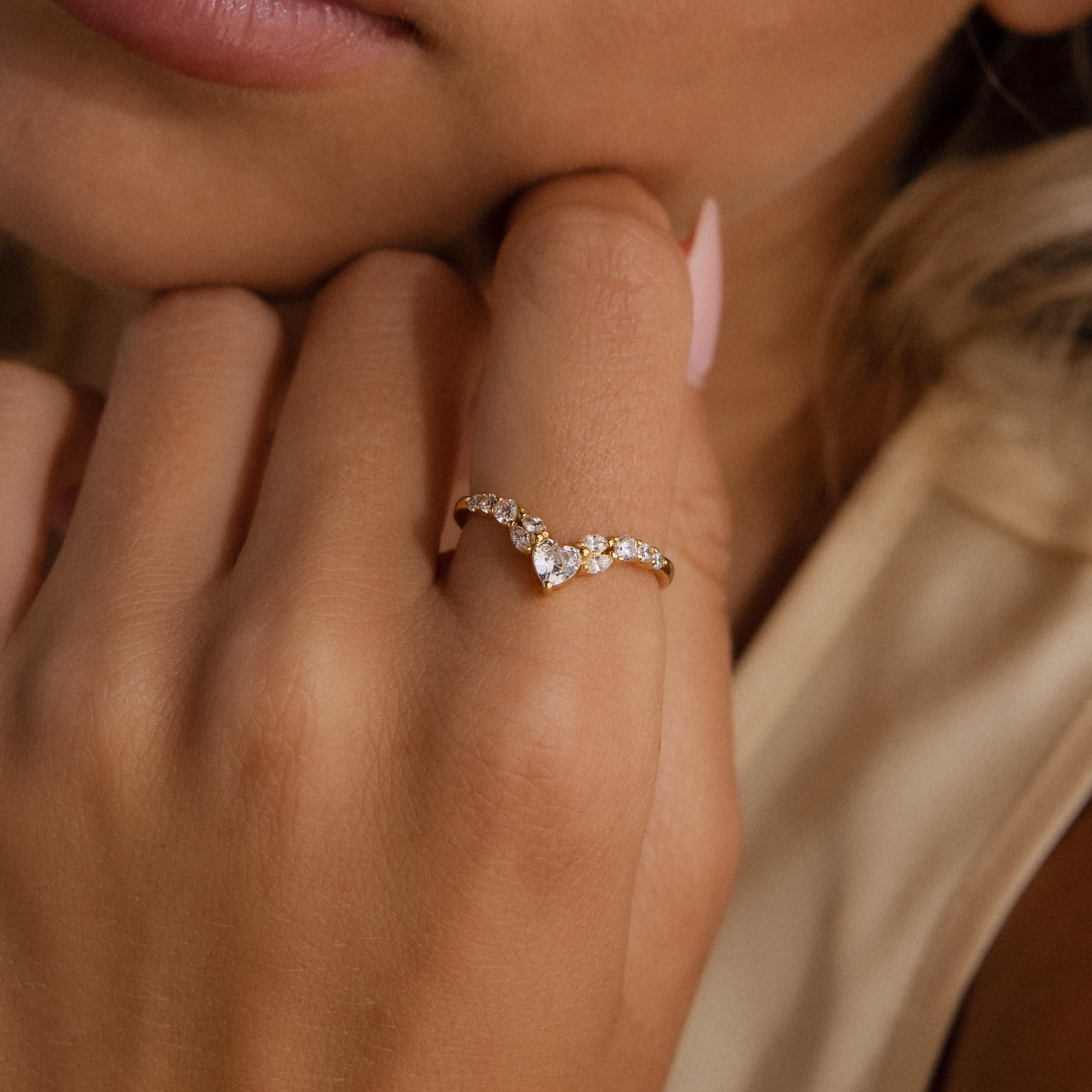 Gold heart curve cluster diamond ring with heart shaped and round diamonds shown on a woman's hand.