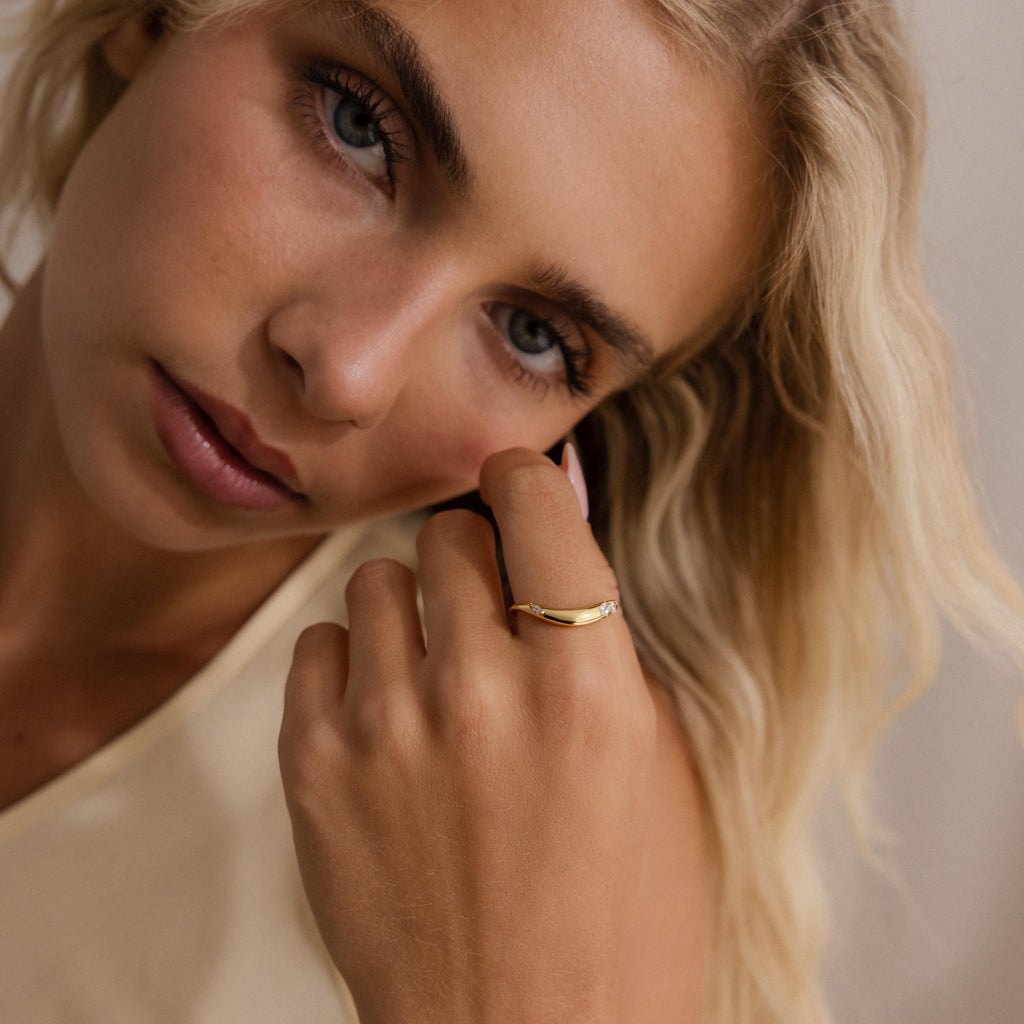 Woman wearing a minimalist gold curved band ring with three marquise cut clear gemstones, styled with a soft natural look.