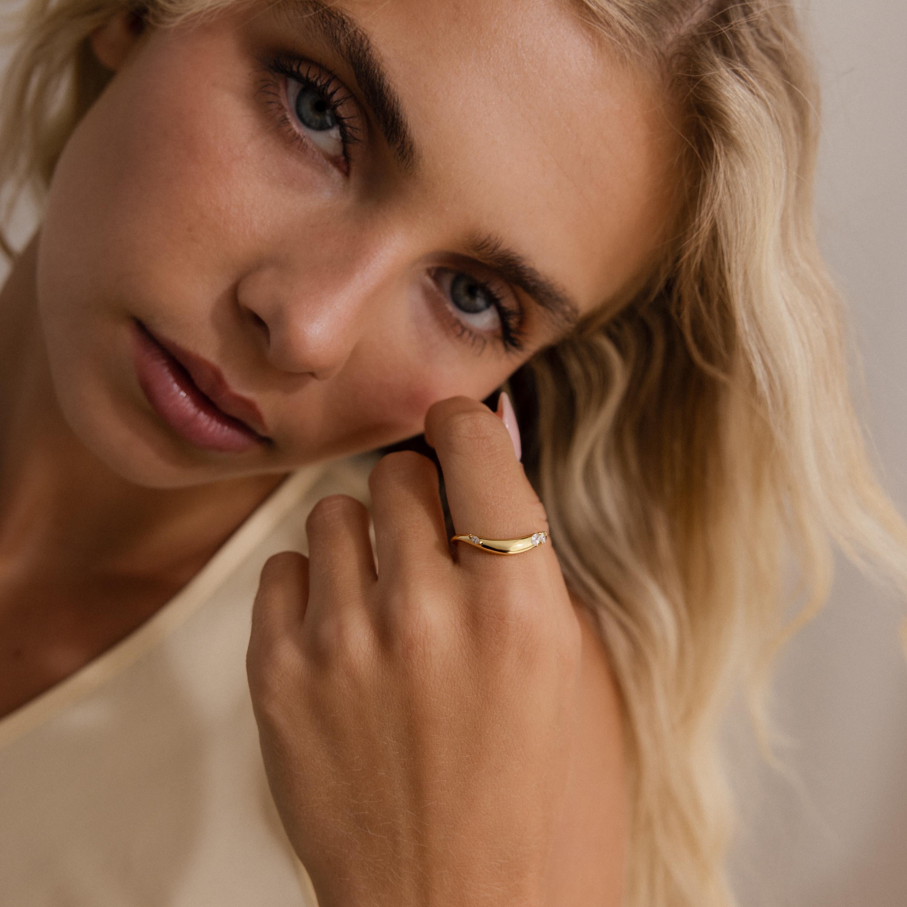 Woman wearing a minimalist gold curved band ring with three marquise cut clear gemstones, styled with a soft natural look.