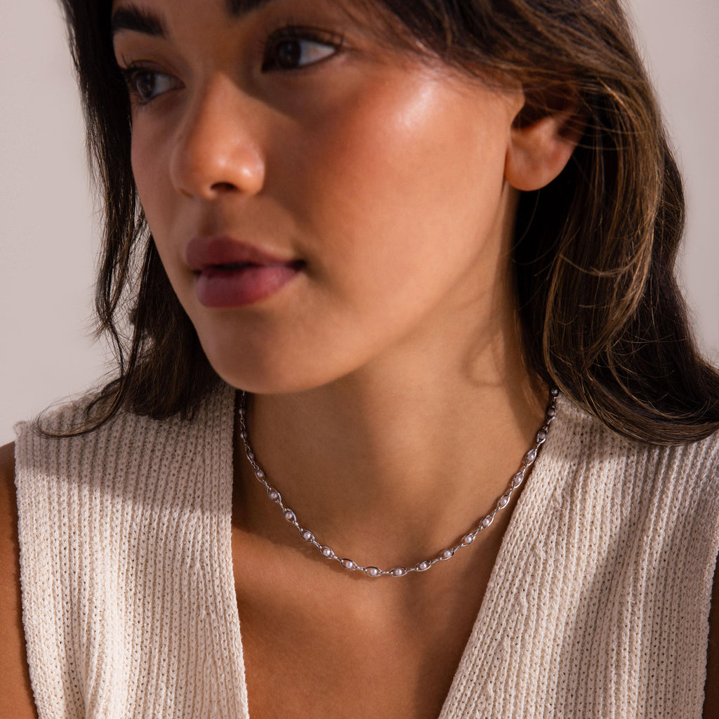 Woman wearing a silver pearl chain necklace, featuring small white pearls evenly spaced along delicate metal links.