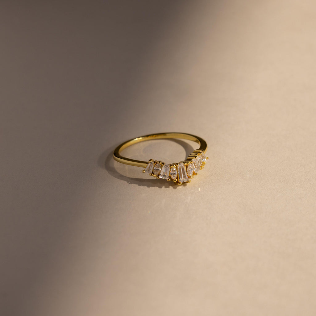 Minimal gold ring with a curved row of baguette and marquise cut clear stones, shown in soft natural light against a neutral background for a modern, elegant presentation.