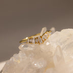 Gold ring with a curved row of baguette and marquise cut clear stones, elegantly displayed resting on raw crystal for a natural and luminous presentation.