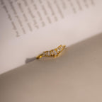 Gold ring with a curved row of baguette and marquise cut clear stones, delicately placed on the crease of an open book for a refined and artistic presentation.
