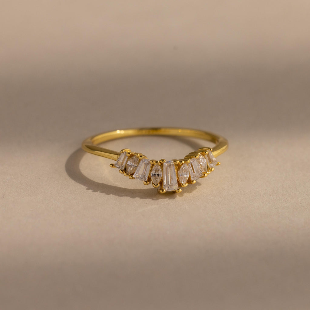 Delicate gold ring with a row of tapered baguette and marquise cut clear gemstones set in a subtle curved design, creating a refined and elegant look.