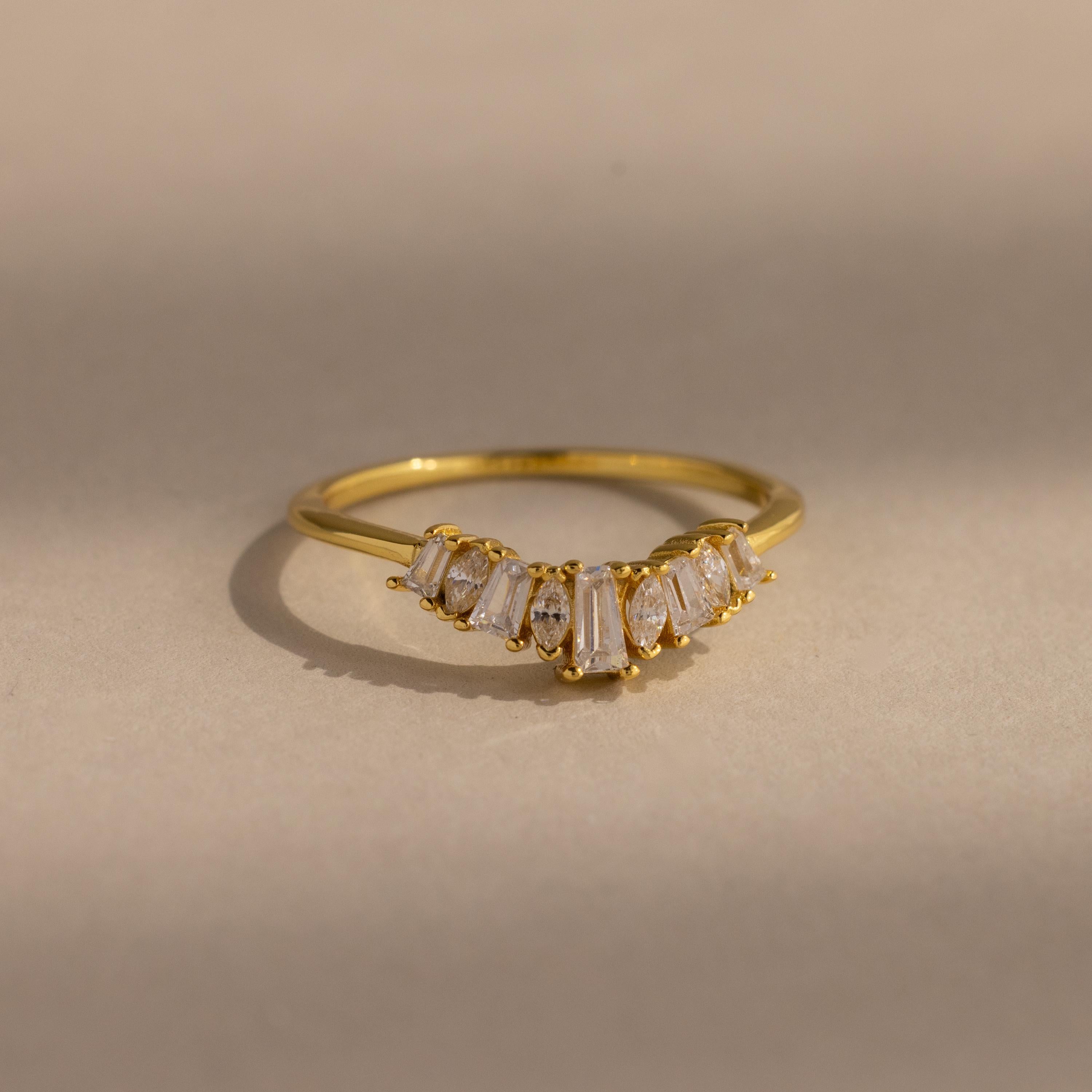 Delicate gold ring with a row of tapered baguette and marquise cut clear gemstones set in a subtle curved design, creating a refined and elegant look.