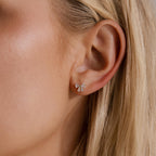 Close up of a woman wearing the Starlight Bow stud earring in gold, featuring baguette cut clear stones arranged in a delicate bow design for an elegant look.