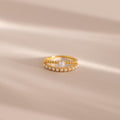 Gold beaded ring set featuring one band with a single central pearl and another adorned with a row of small pearls, displayed on a neutral beige surface with soft light shadows.