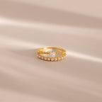 Gold beaded ring set featuring one band with a single central pearl and another adorned with a row of small pearls, displayed on a neutral beige surface with soft light shadows.