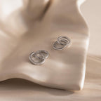 Pair of silver interlocking hoop earrings, one encrusted with small clear stones, displayed on a smooth, cream colored shell like surface.