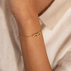 Gold chain bracelet with two interlocking oval links at the center, one link polished and the other encrusted with small clear stones, worn on the wrist.