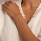 Woman wearing a delicate silver chain bracelet featuring an interlocking loop design, with one loop adorned with small clear stones, paired with a soft cream collared top.