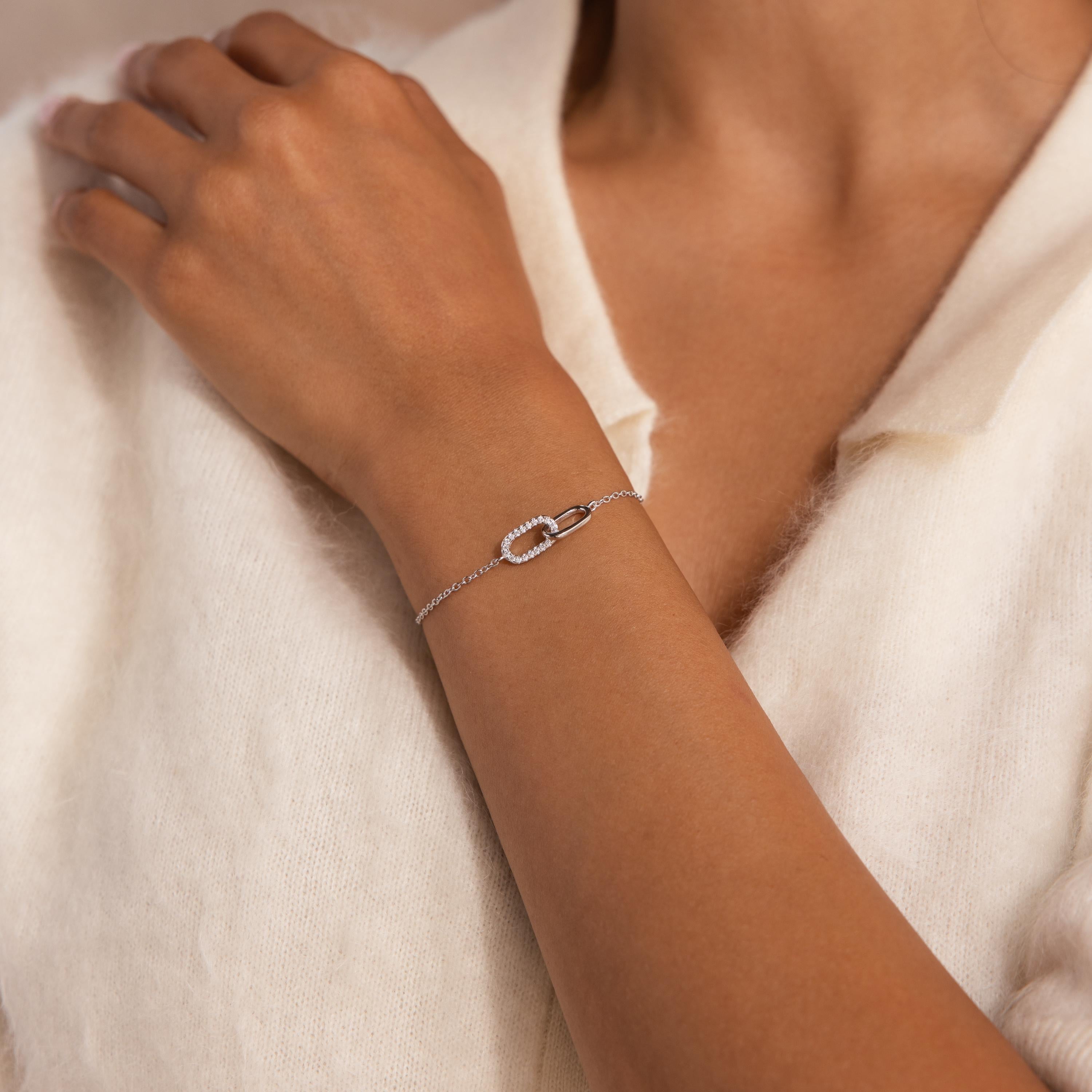 Woman wearing a delicate silver chain bracelet featuring an interlocking loop design, with one loop adorned with small clear stones, paired with a soft cream collared top.