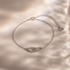Delicate silver chain bracelet with two interlocking oval links at the center, one polished and one encrusted with small clear stones, displayed on a softly lit neutral background.