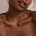 Woman wearing a silver necklace with a square black onyx pendant framed in silver, styled against bare skin with a neutral background.