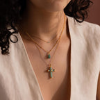 A woman styles the Jade Cross Necklace, featuring natural jade pendants, with other layered gold-tone necklaces and a V-neck beige top.