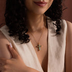 Woman wearing a gold chain necklace with a jade cross pendant, accented with gold end caps and an X-shaped detail at the center, styled with a cream V-neck top.